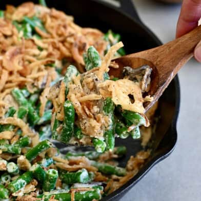 Scooping green bean casserole made from scratch from a skillet.