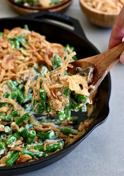 Scooping green bean casserole made from scratch from a skillet.