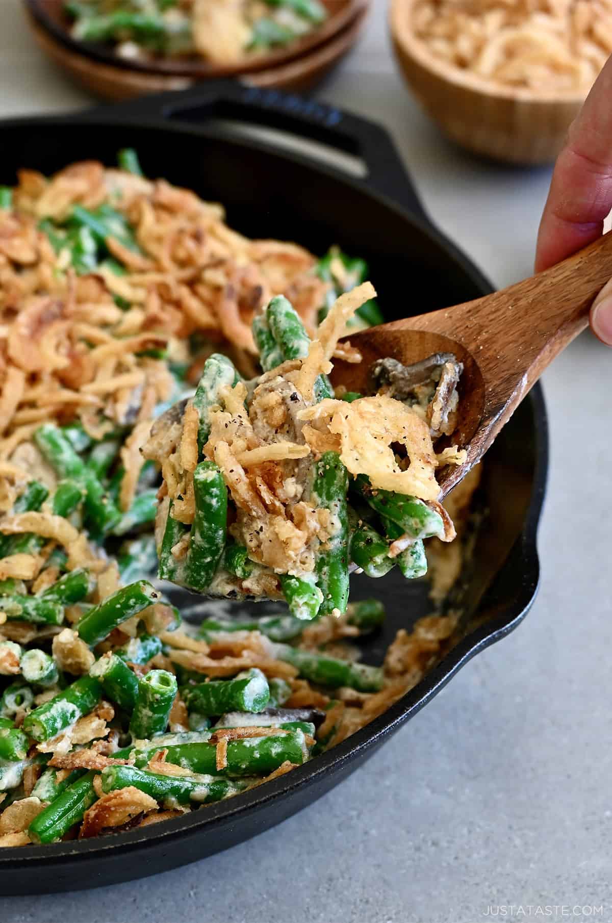 Scooping green bean casserole made from scratch from a skillet.
