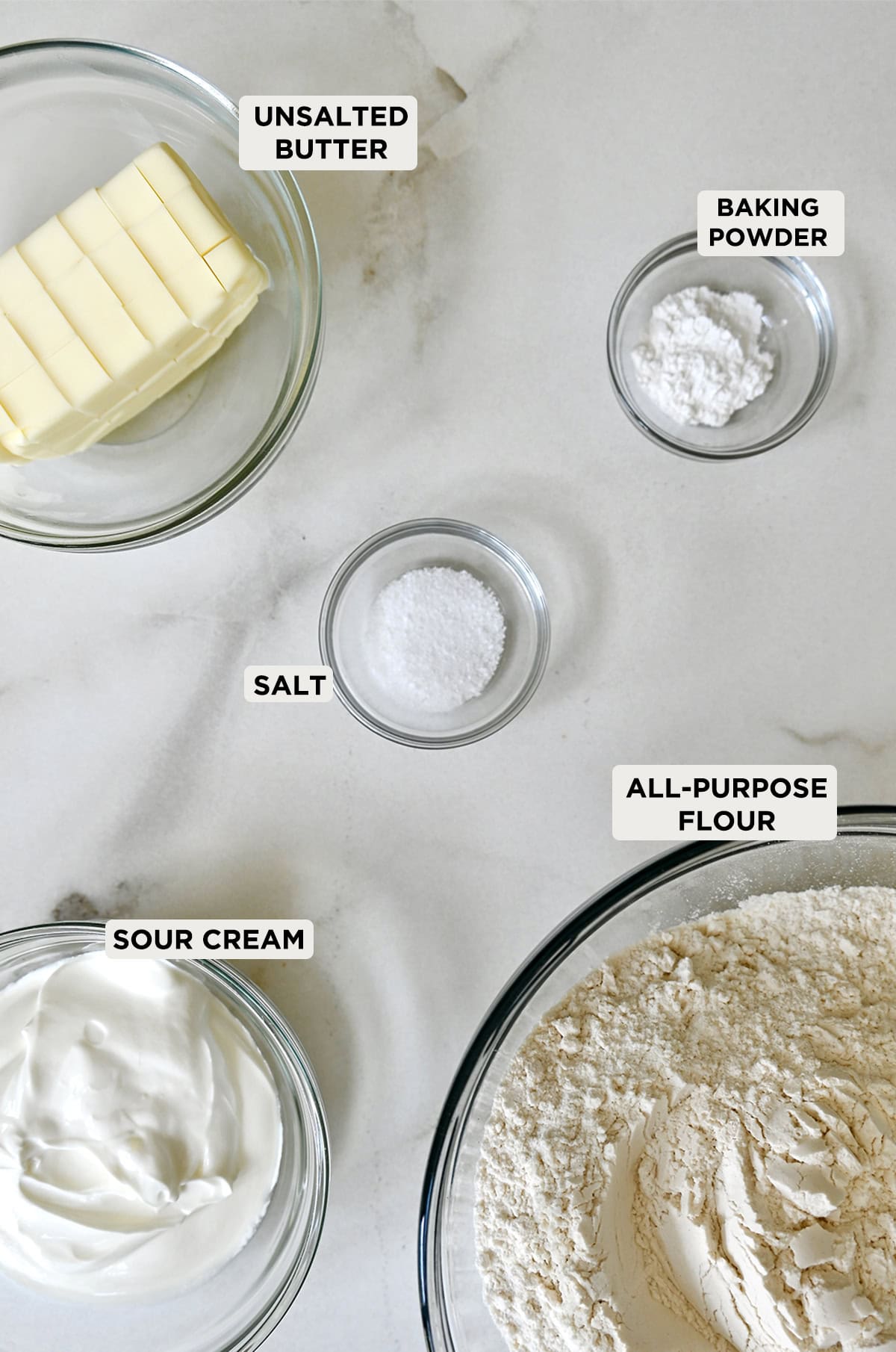 Pie crust ingredients in glass bowls, including butter, sour cream, salt, baking powder and all-purpose flour.