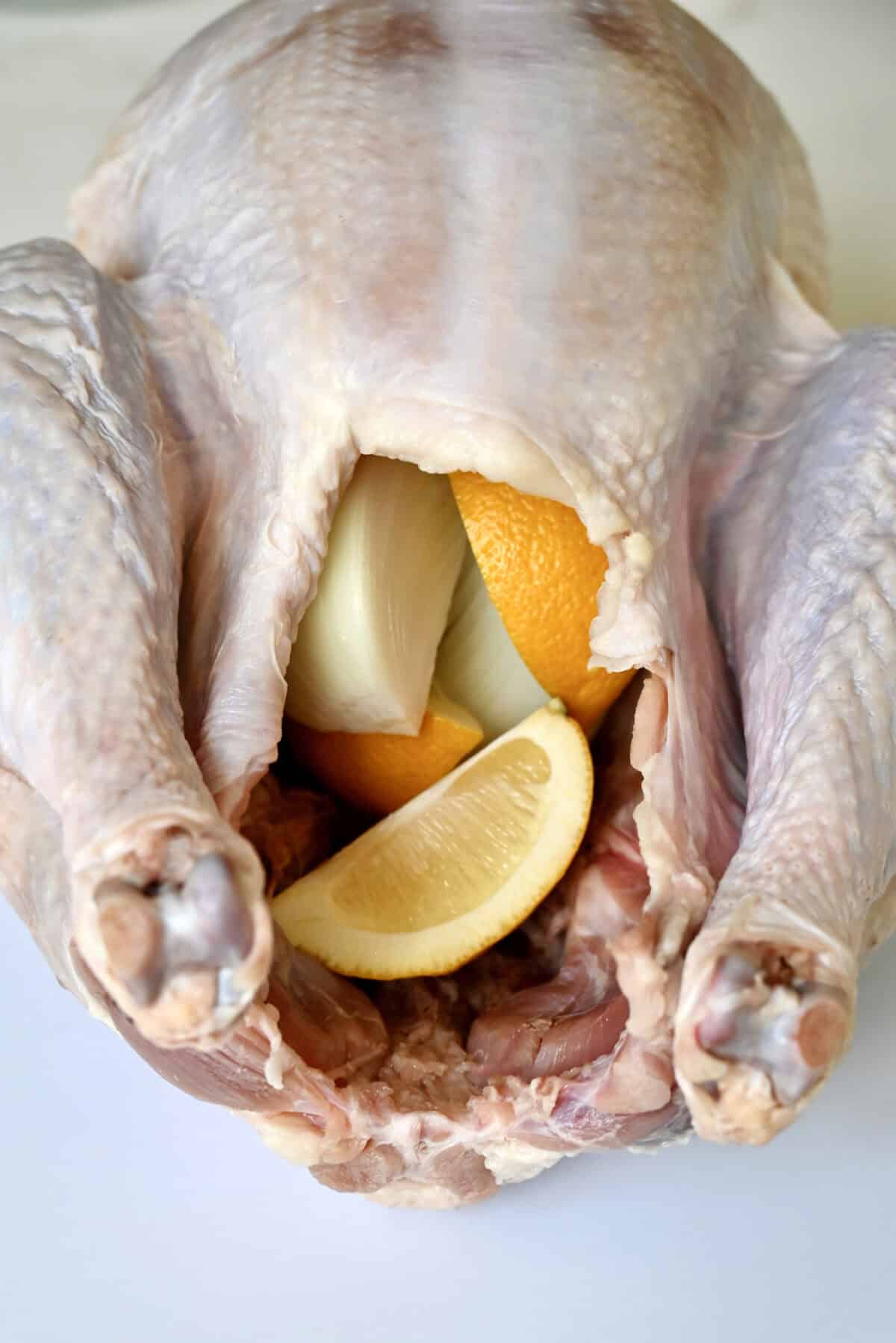 Uncooked turkey with sliced onion and lemons inside the cavity.