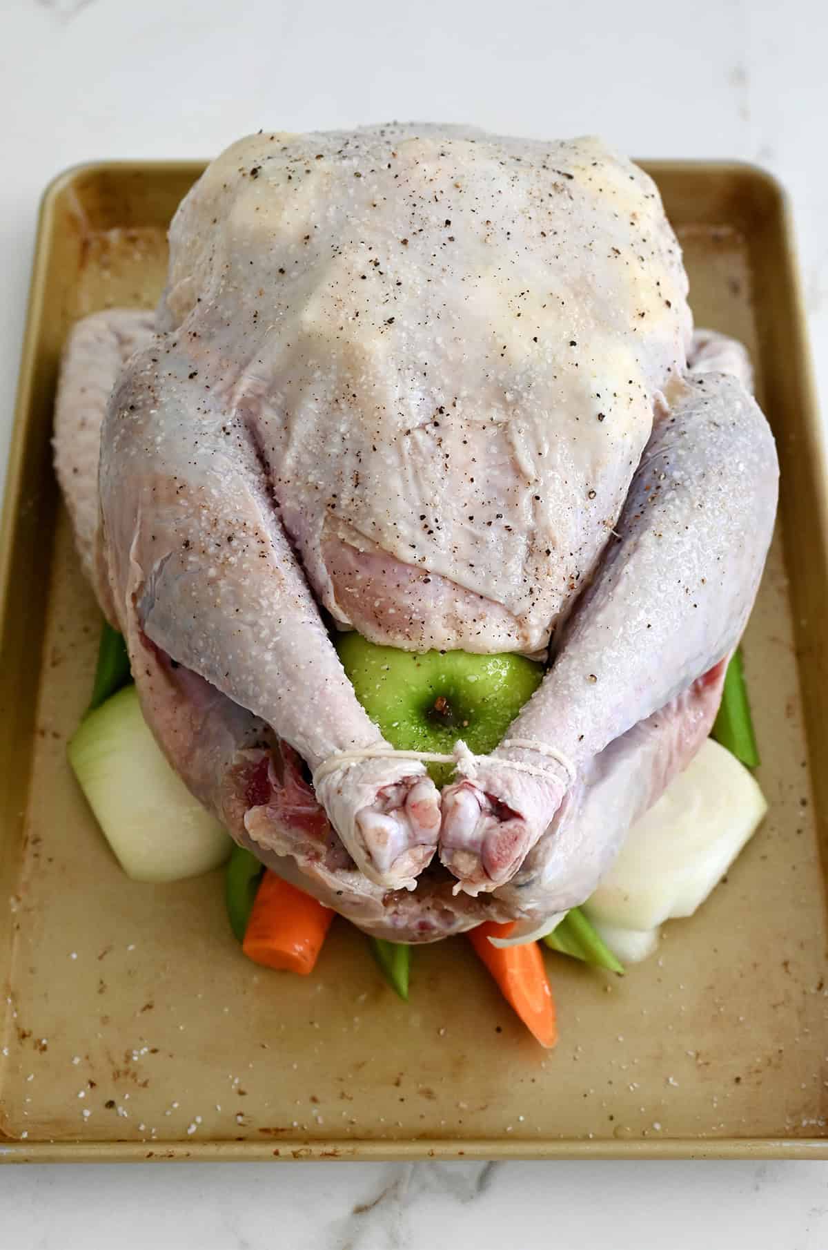 An uncooked turkey atop chopped veggies on a baking tray before roasting.