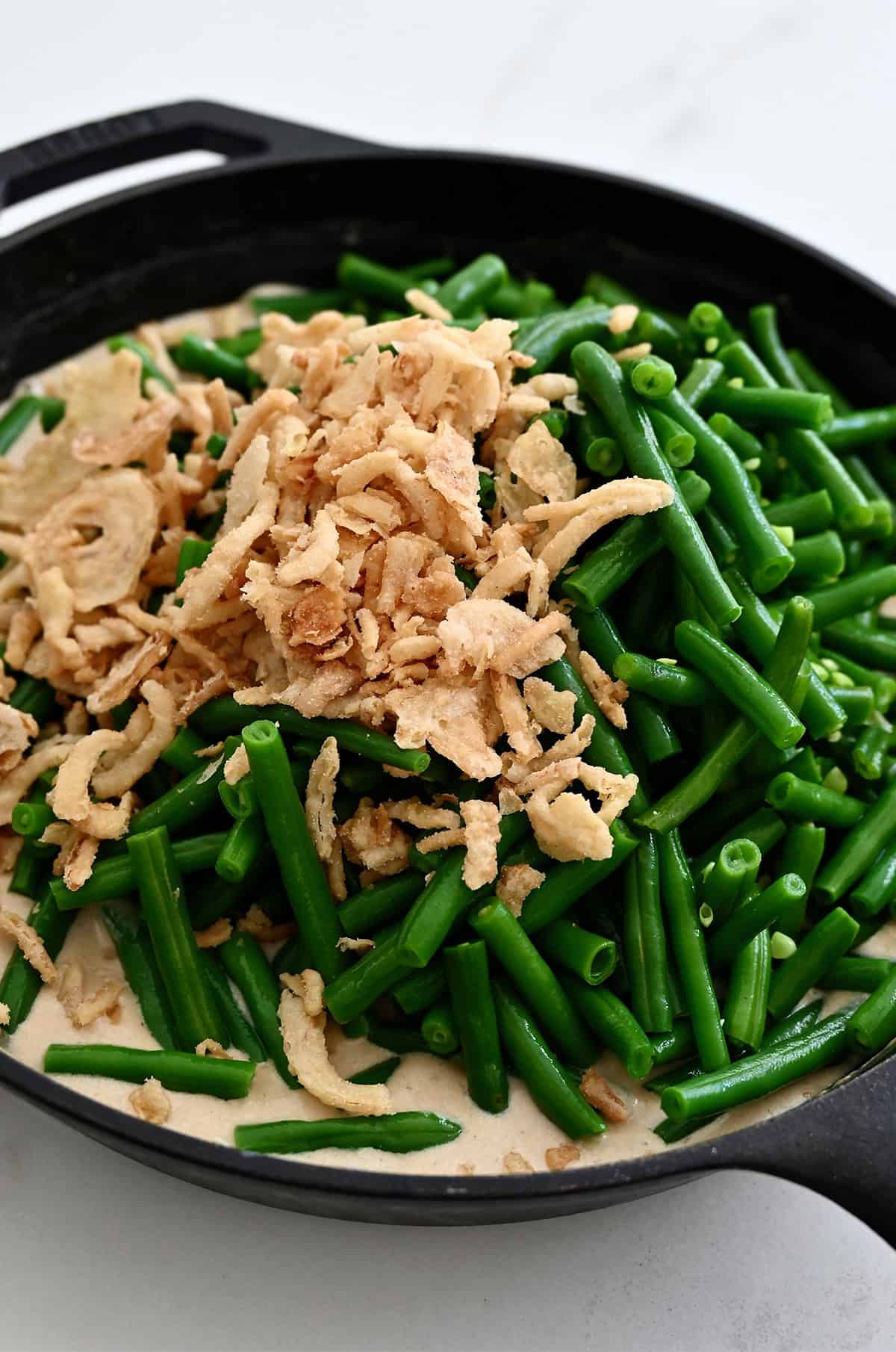 Green beans and crispy fried onions atop homemade cream of mushroom soup in a skillet.