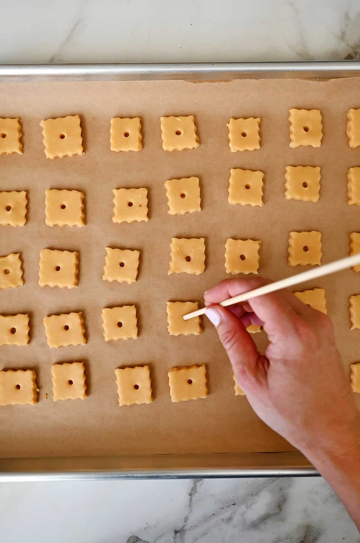 Using the bottom of a bamboo skewer to poke holes into the center of cheese crackers to look like Cheez-Its.