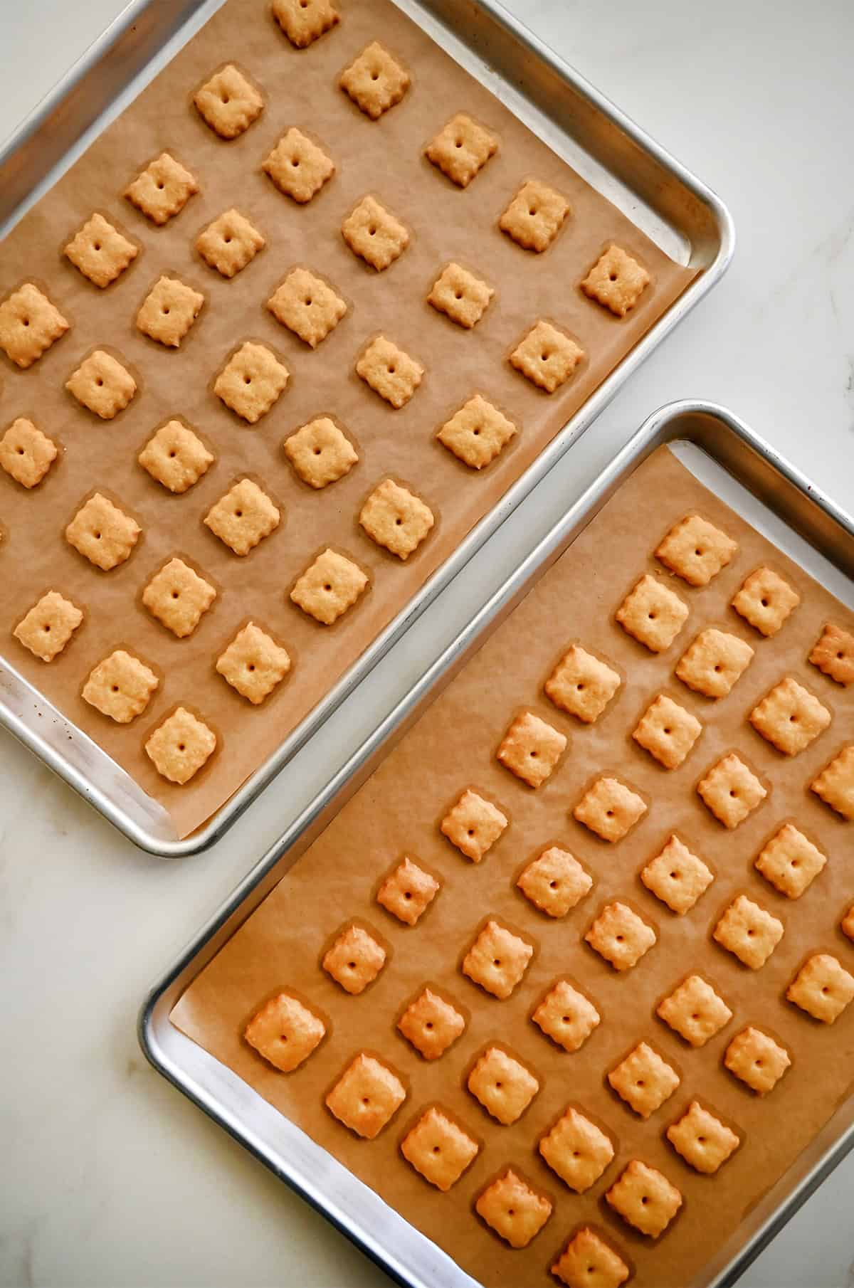 Baked cheese crackers cooling on baking sheets lined with parchment paper.