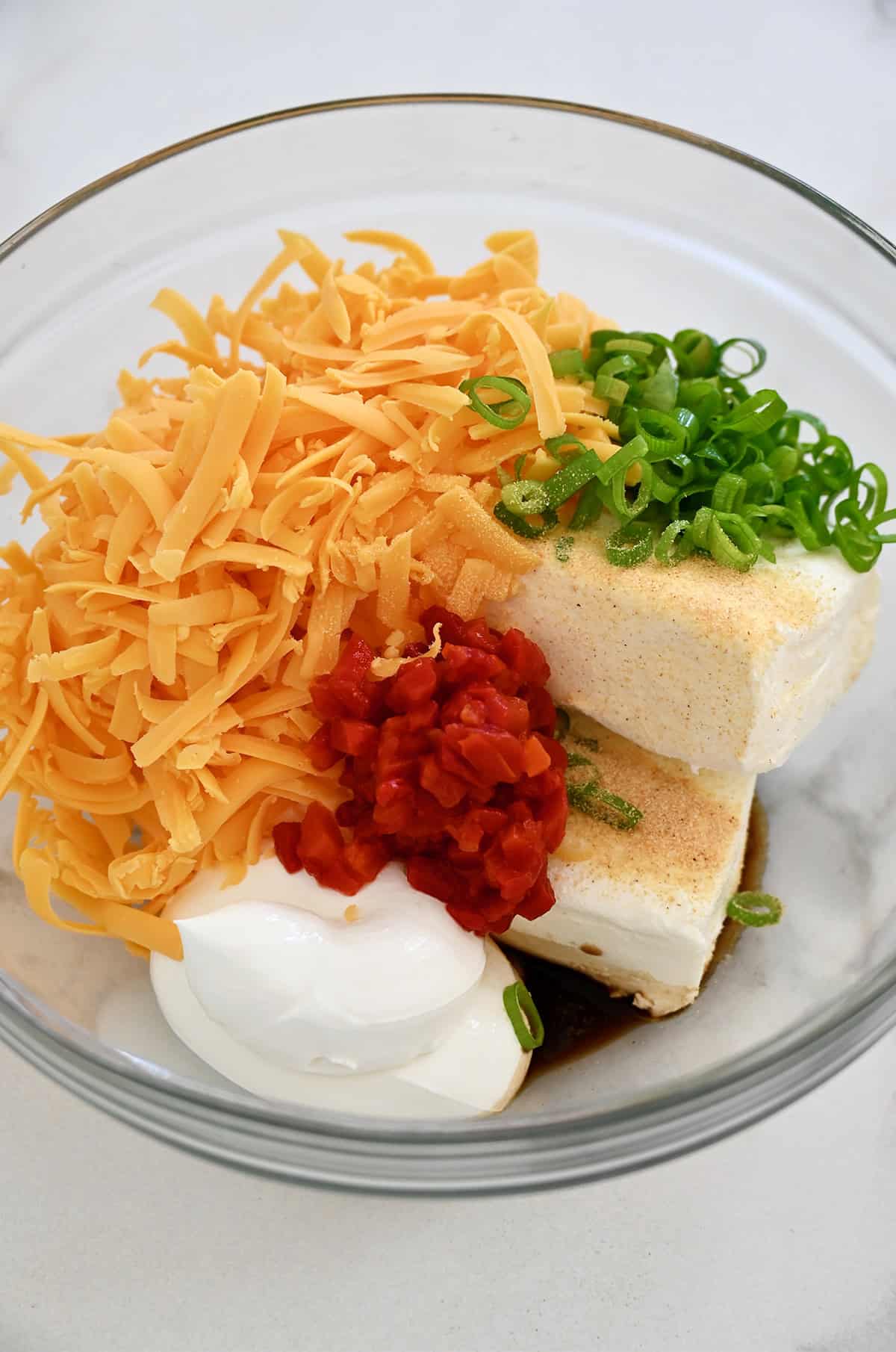 Cream cheese, sour cream, shredded cheddar, chopped scallions, pimiento peppers, garlic powder and Worcestershire sauce in a glass bowl.