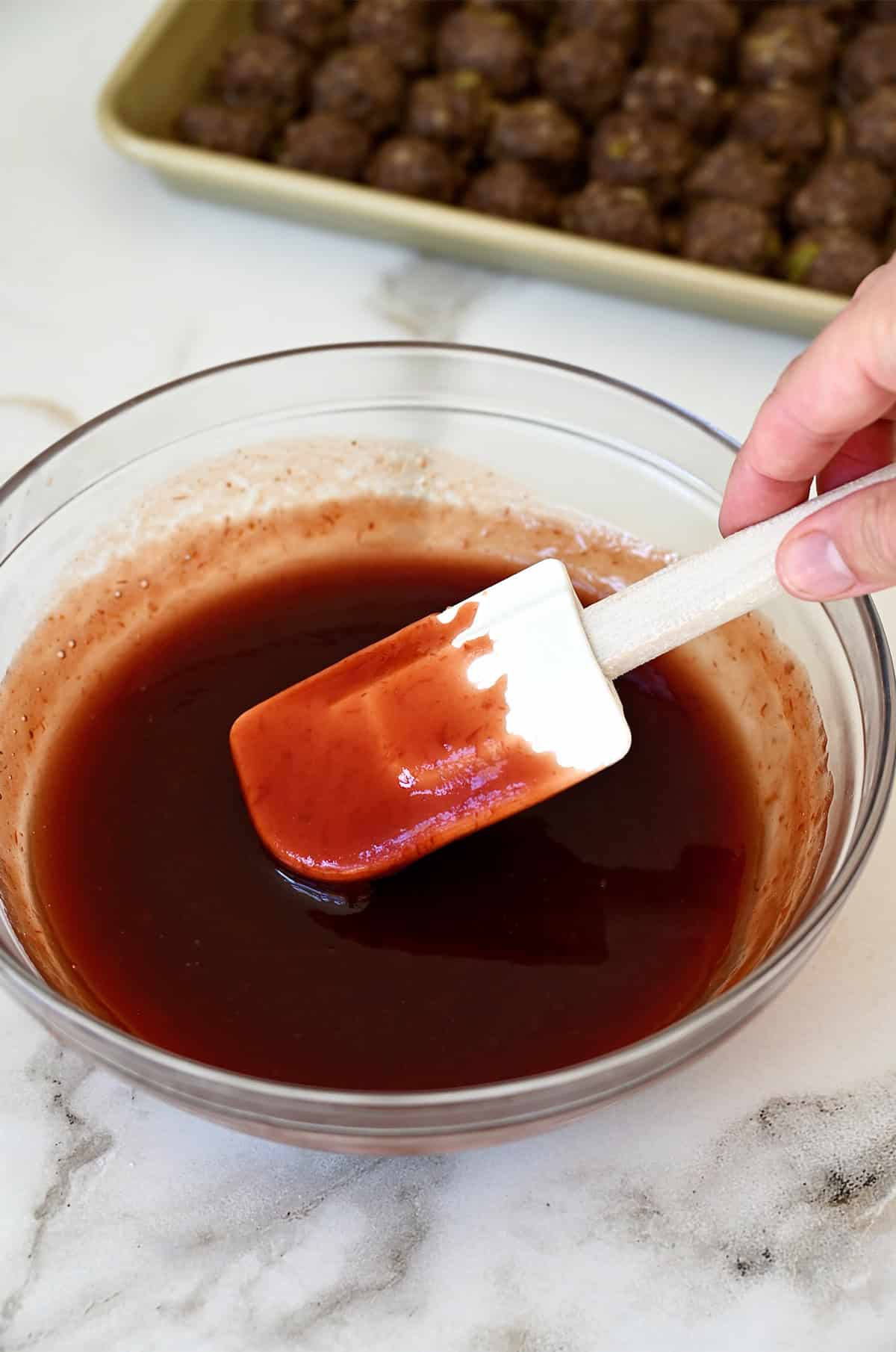 Grape jelly and chili sauce in a  bowl and coating a spatula.
