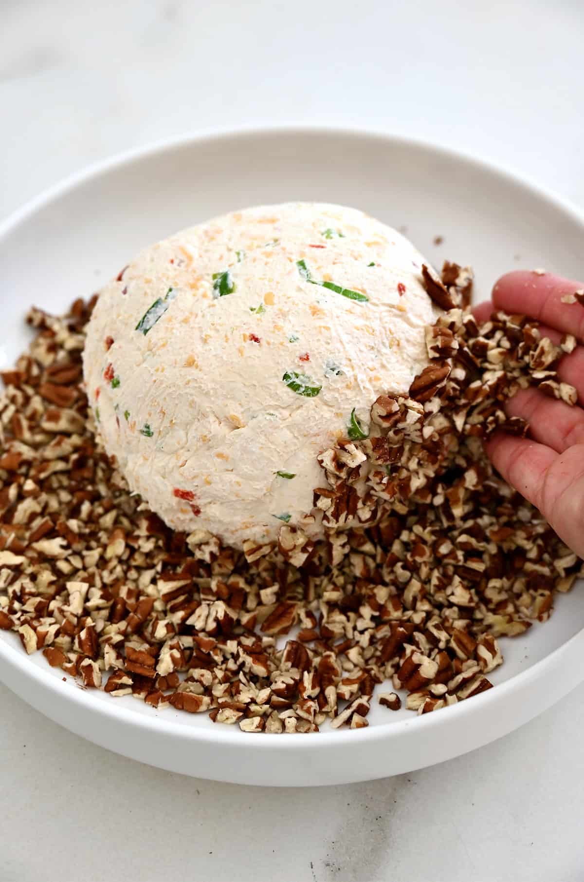 A cheeseball sits atop crushed pecans on a plate.