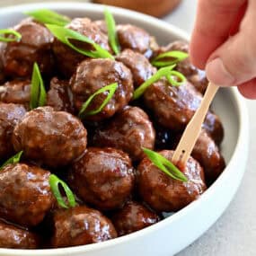 Grape jelly cocktail meatballs in a bowl with toothpicks nearby for serving.
