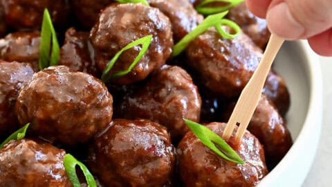 Grape jelly cocktail meatballs in a bowl with toothpicks nearby for serving.