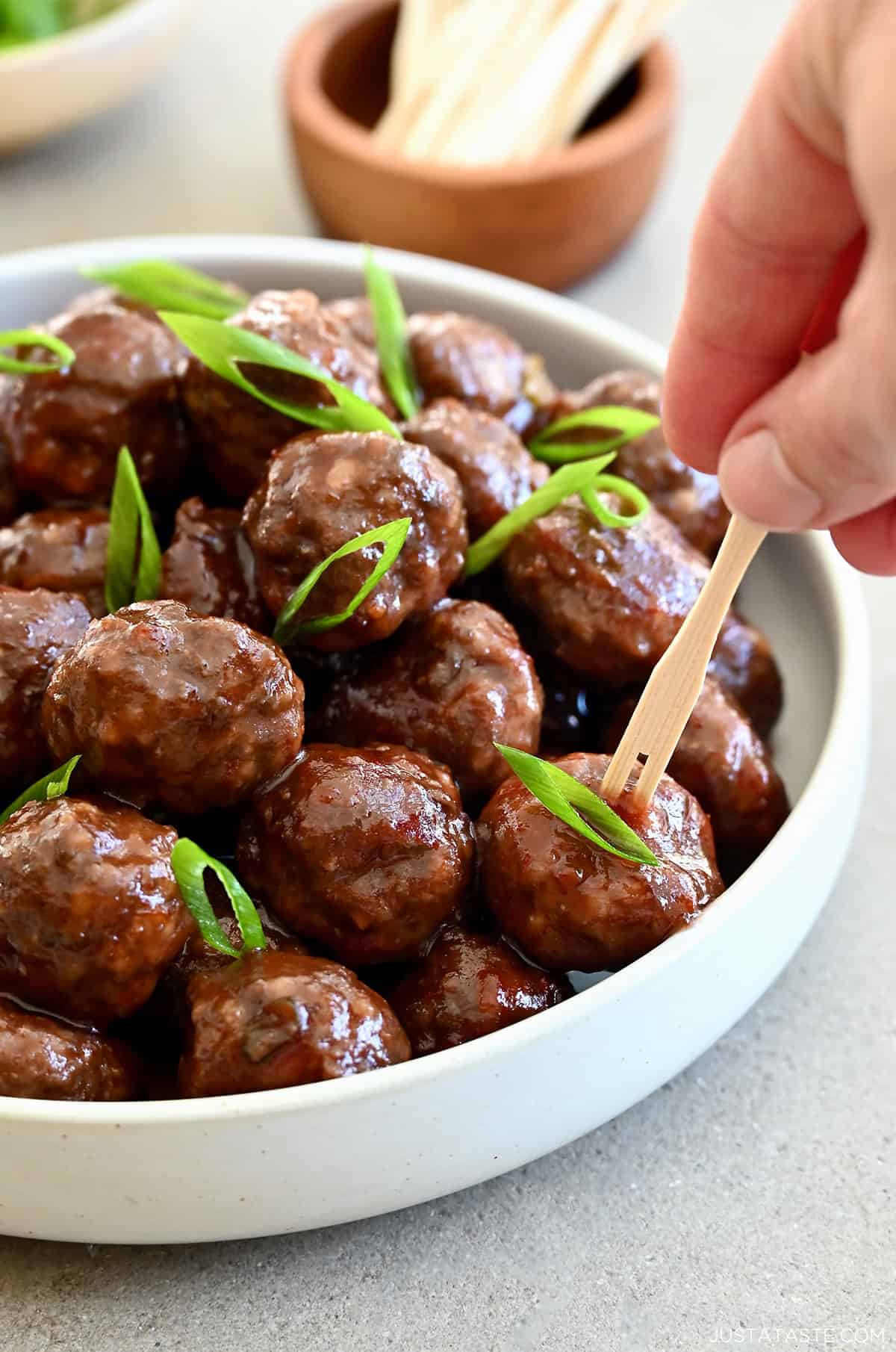 Grape jelly cocktail meatballs in a bowl with toothpicks nearby for serving.