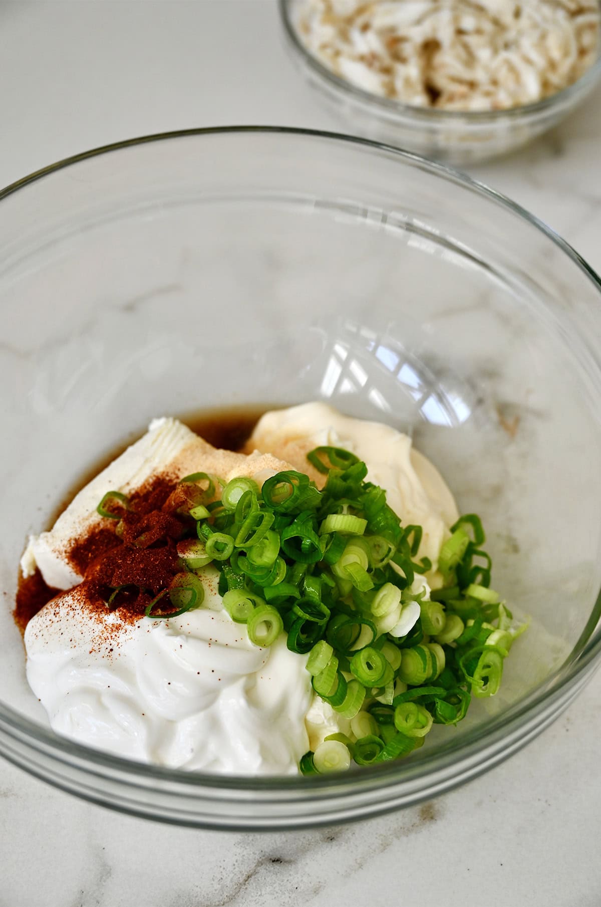 A glass bowl containing mayonnaise, sour cream, cream cheese, sliced scallions, Worcestershire sauce and paprika.