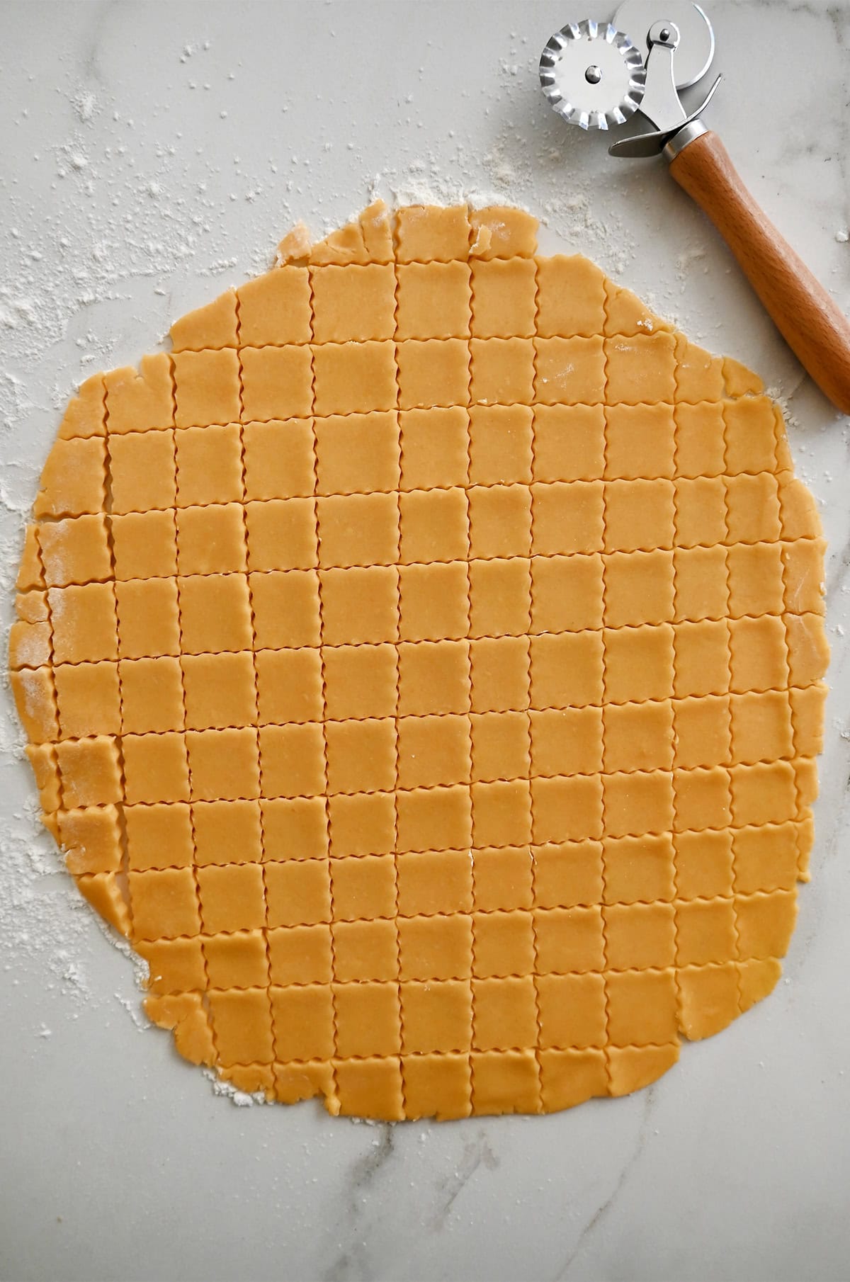 Cutting cheese cracker dough into squares with a fluted pastry wheel.