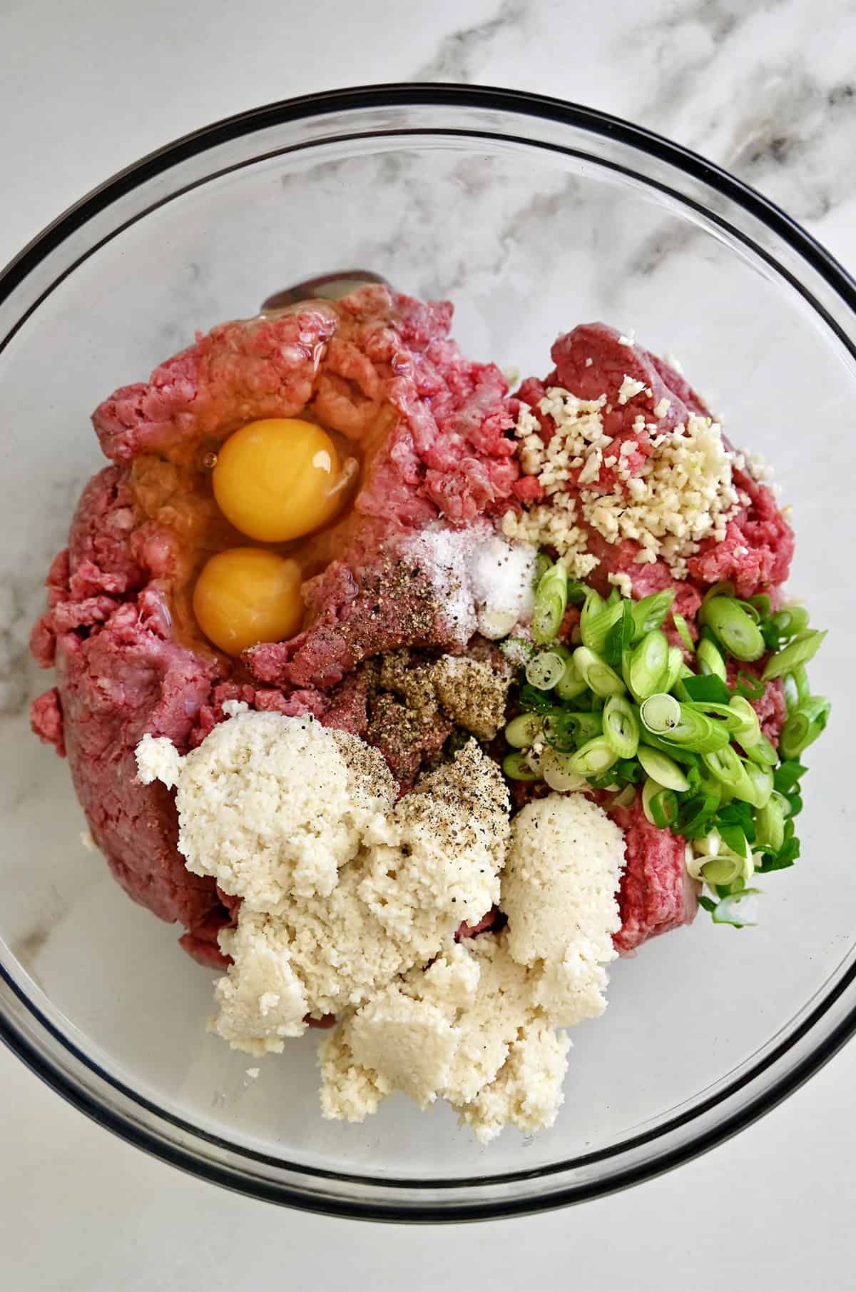 Panade, ground beef, eggs, minced garlic, sliced scallions, salt and pepper in a glass bowl.