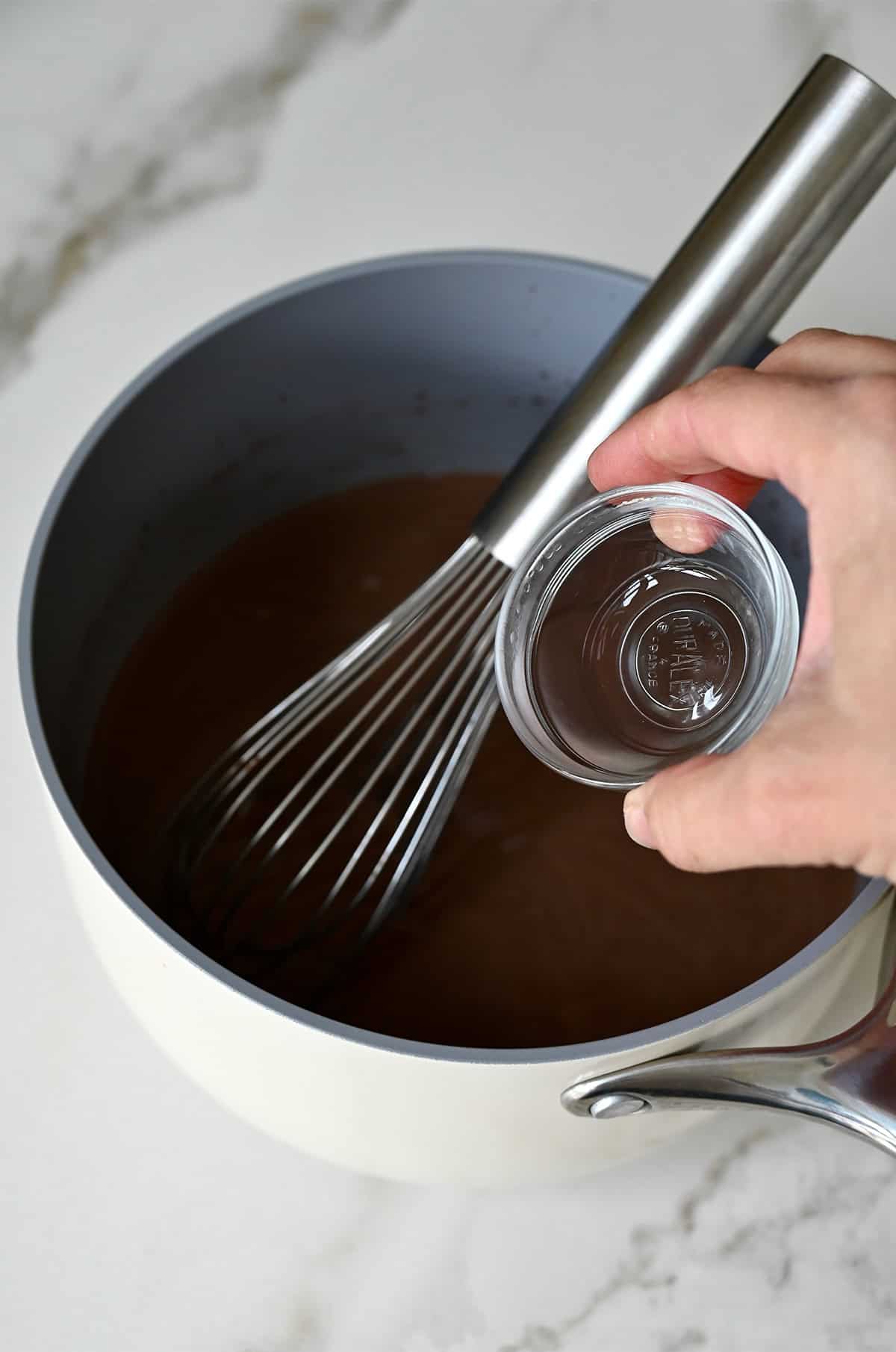 Mint extract being added to a mocha mixture in a saucepan.