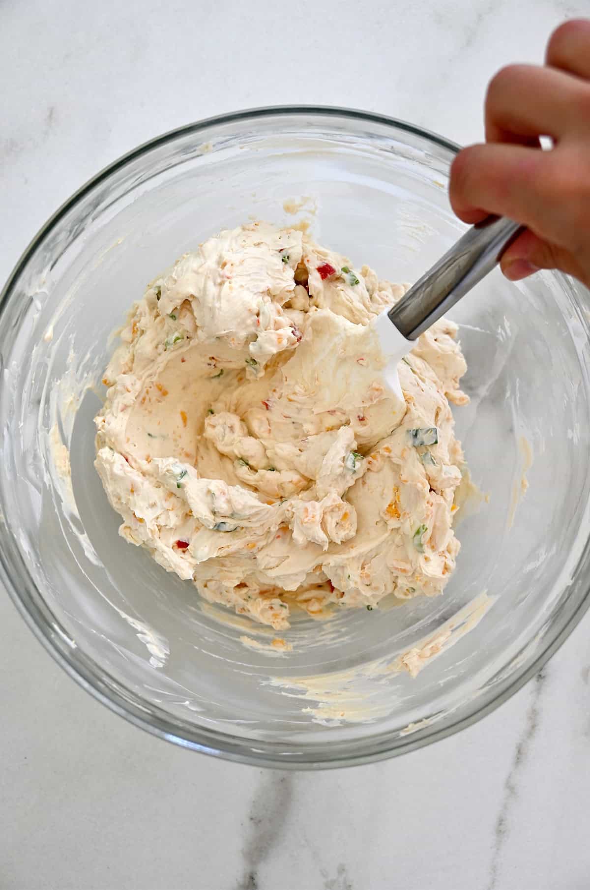 Cheese mixture in a glass bowl with a spatula.