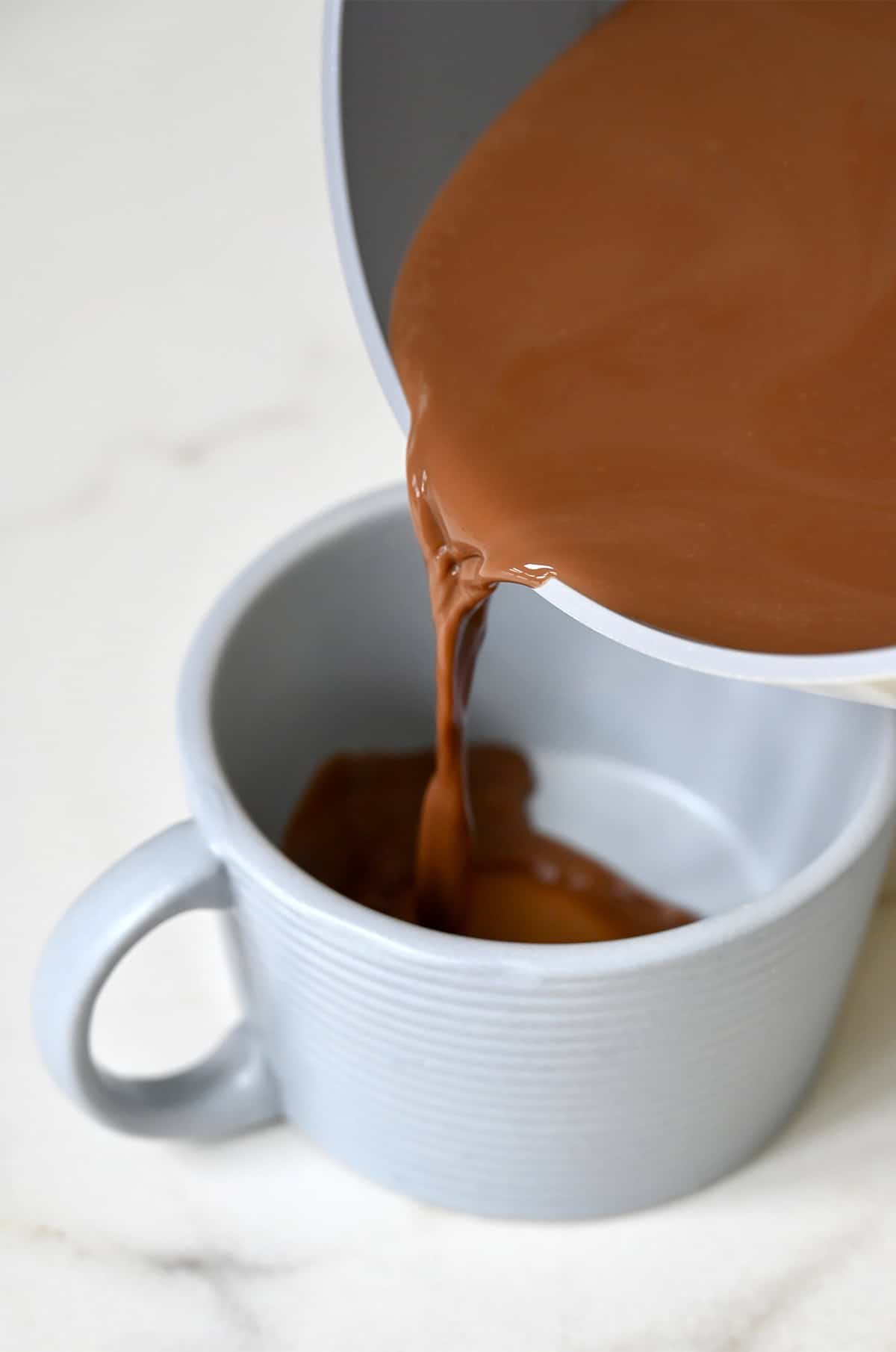 Pouring homemade mocha from a saucepan into a mug.