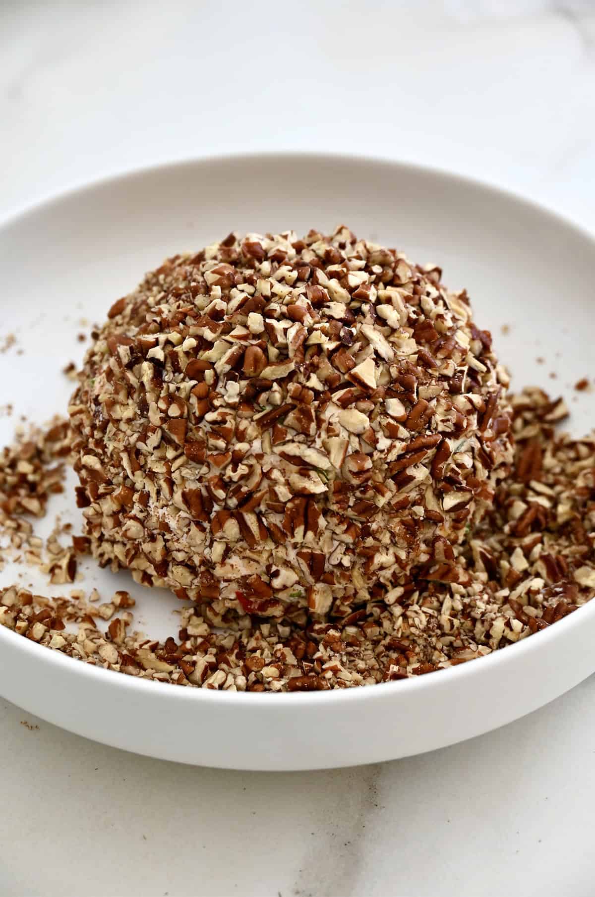 A cheese ball coated in chopped pecans on a shallow plate. 