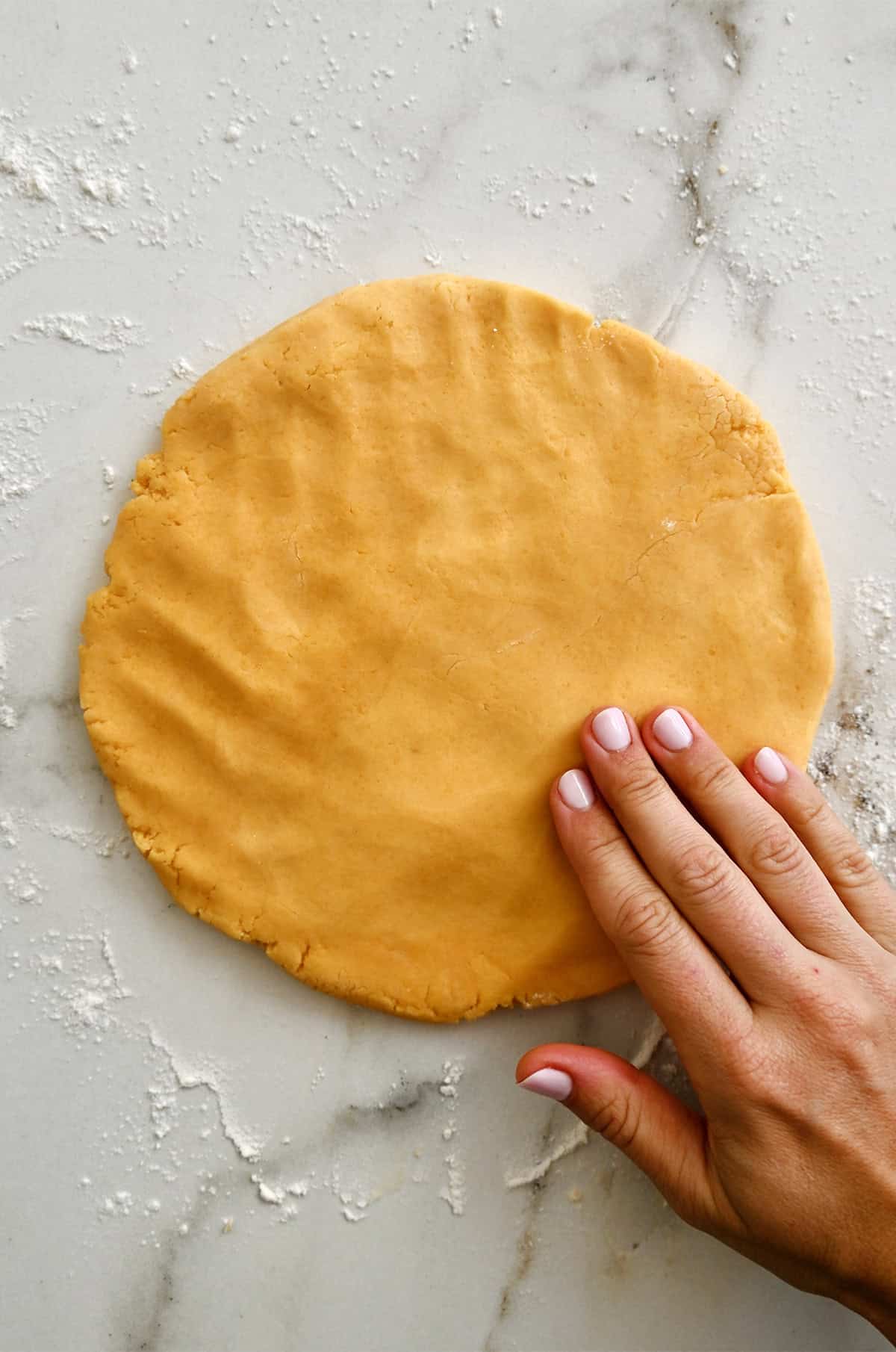 Shaping cheddar cheese cracker dough into a disk on a lightly floured surface.
