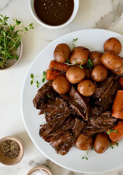 Shredded pot roast with potatoes and carrots on a serving platter with fresh herbs.