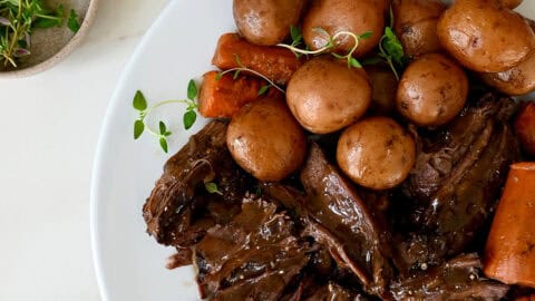 Shredded pot roast with potatoes and carrots on a serving platter with fresh herbs.