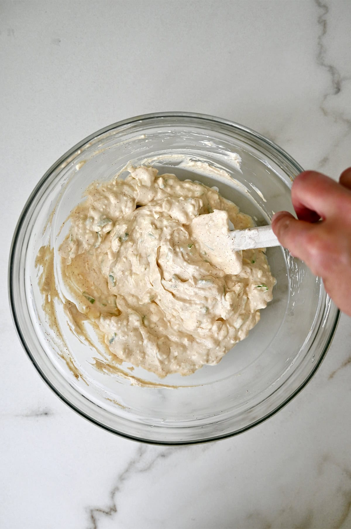 A glass bowl containing the cheesy base for baked crab dip.