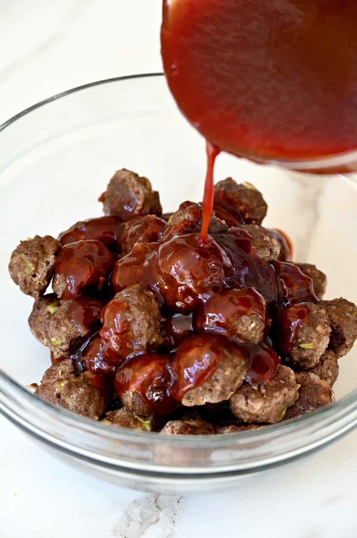 Tossing baked meatballs with grape jelly sauce in a bowl.