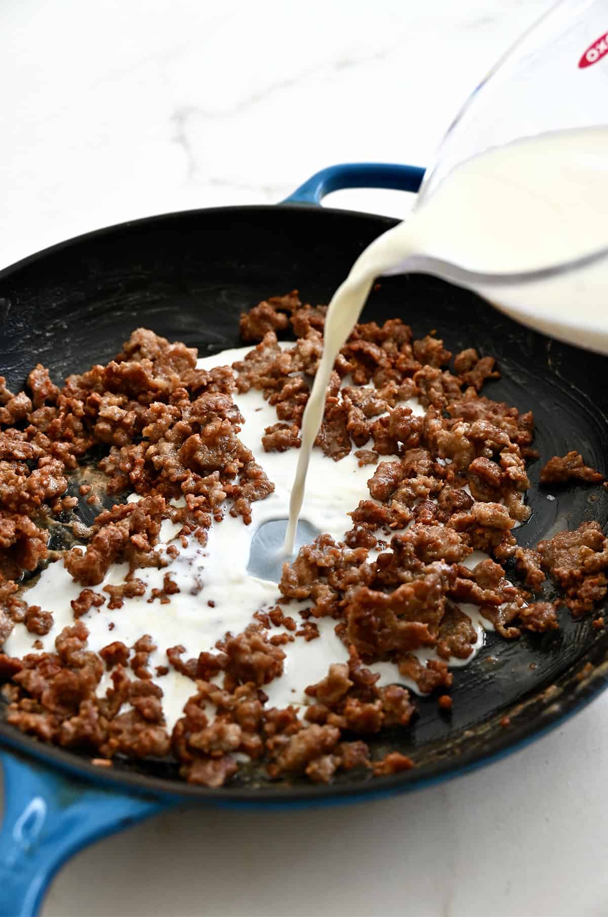 Streaming milk into a skillet with cooked breakfast sausage that's been coated in flour.
