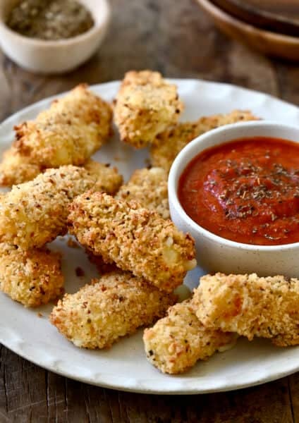 Homemade air fryer mozzarella sticks on a plate with a small bowl containing marinara sauce.