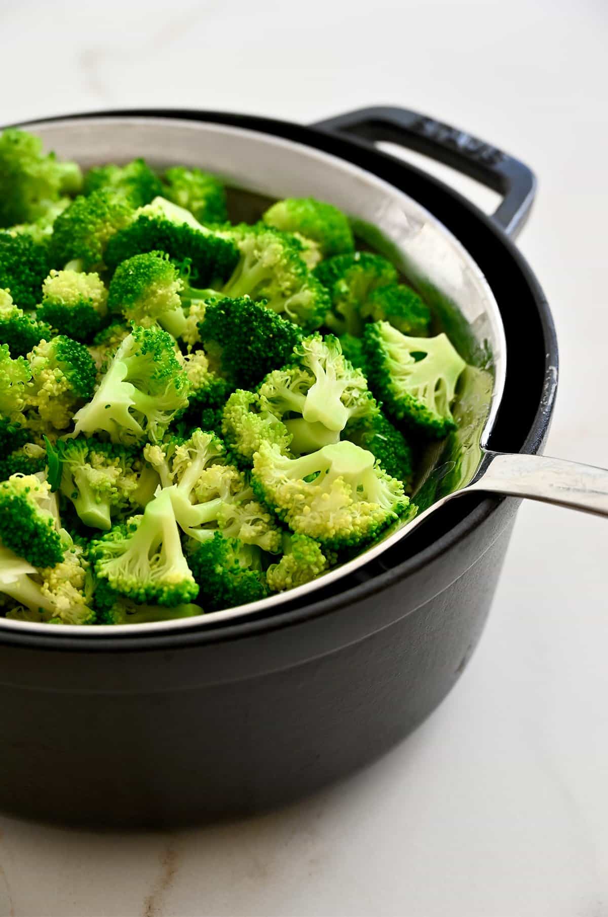 Blanched broccoli florets in a metal sieve over a pot.