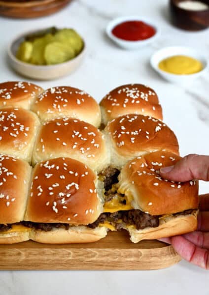 Pull-apart cheeseburger sliders on Hawaiian rolls with a bowl filled with pickles nearby.