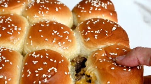 Pull-apart cheeseburger sliders on Hawaiian rolls with a bowl filled with pickles nearby.