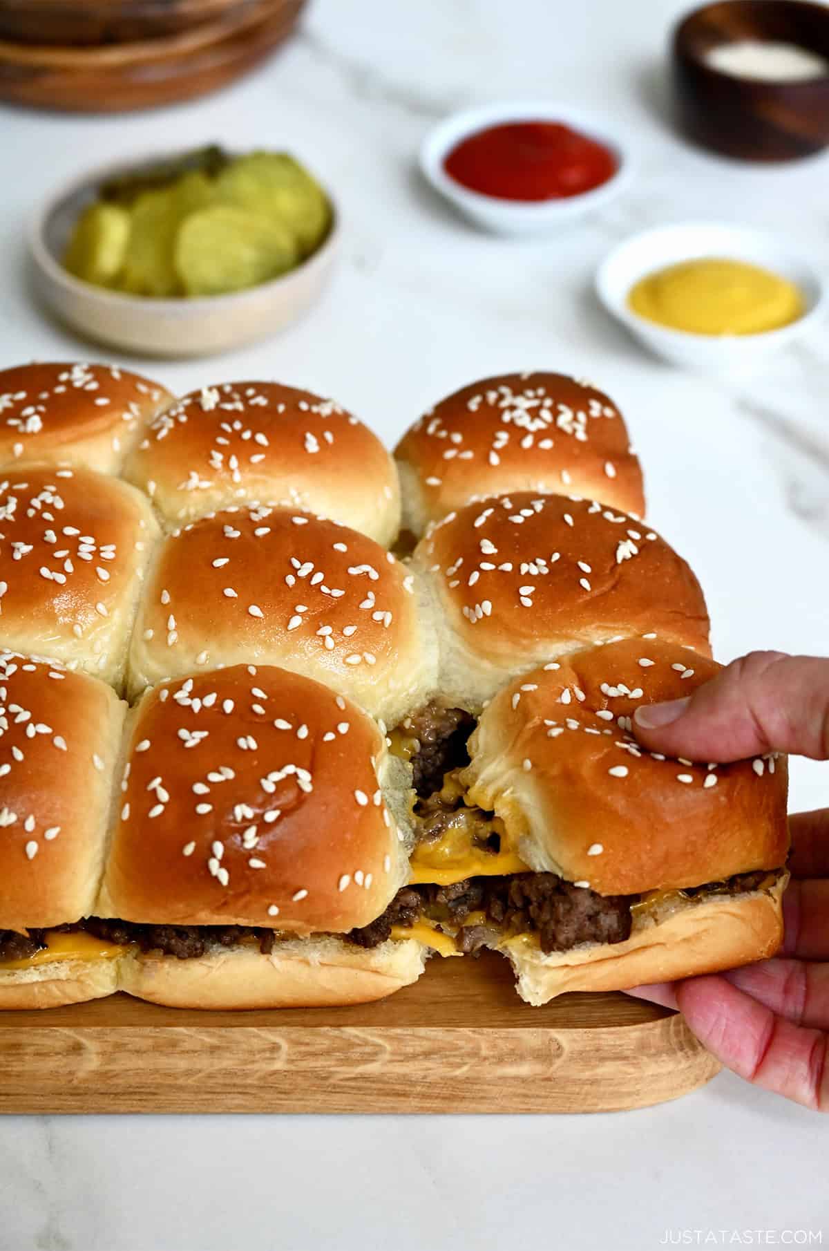 Pull-apart cheeseburger sliders on Hawaiian rolls with a bowl filled with pickles nearby.