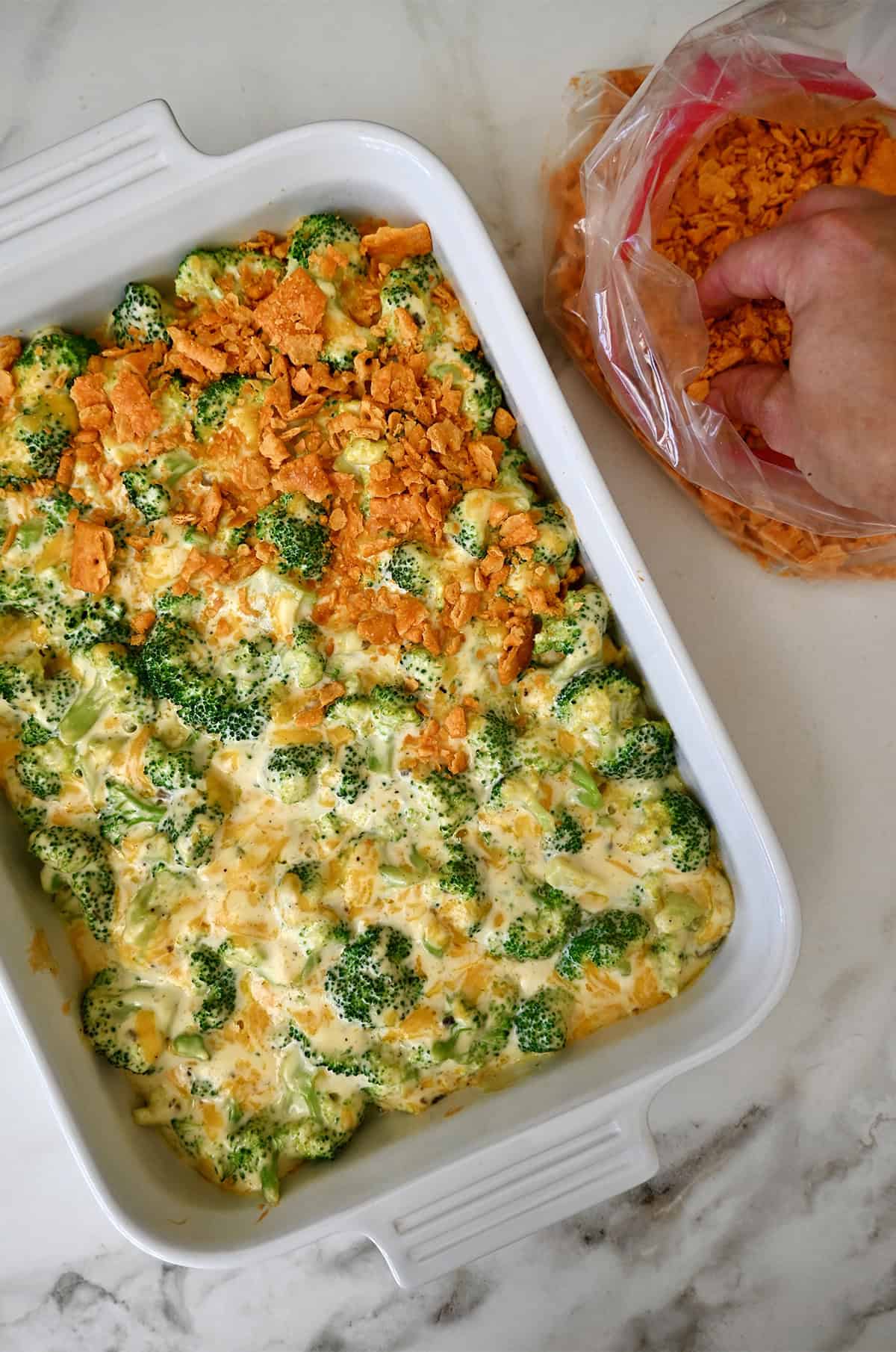 Baked broccoli casserole being topped with crushed cheese crackers.