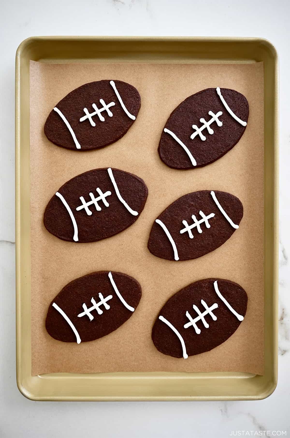 Chocolate football cookies with white laces on a parchment paper-lined baking sheet.
