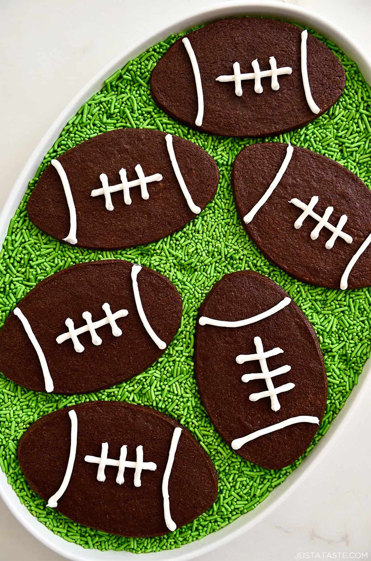Chocolate football sugar cookies on a bed of green sprinkle