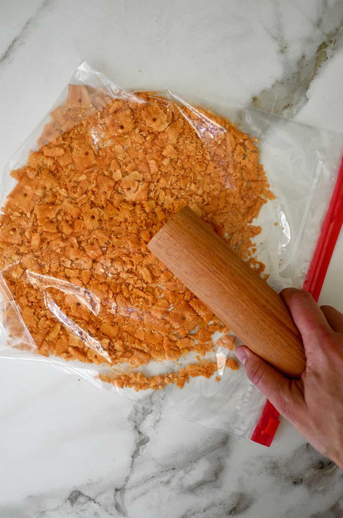 Crushing cheese crackers in a sealed plastic bag with a rolling pin.
