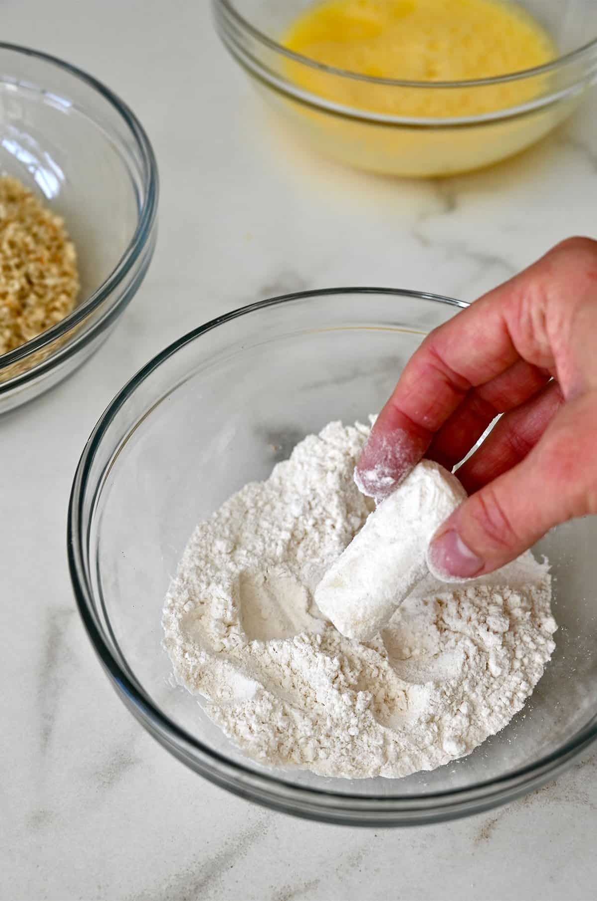 Dredging a mozzarella cheese stick in flour.