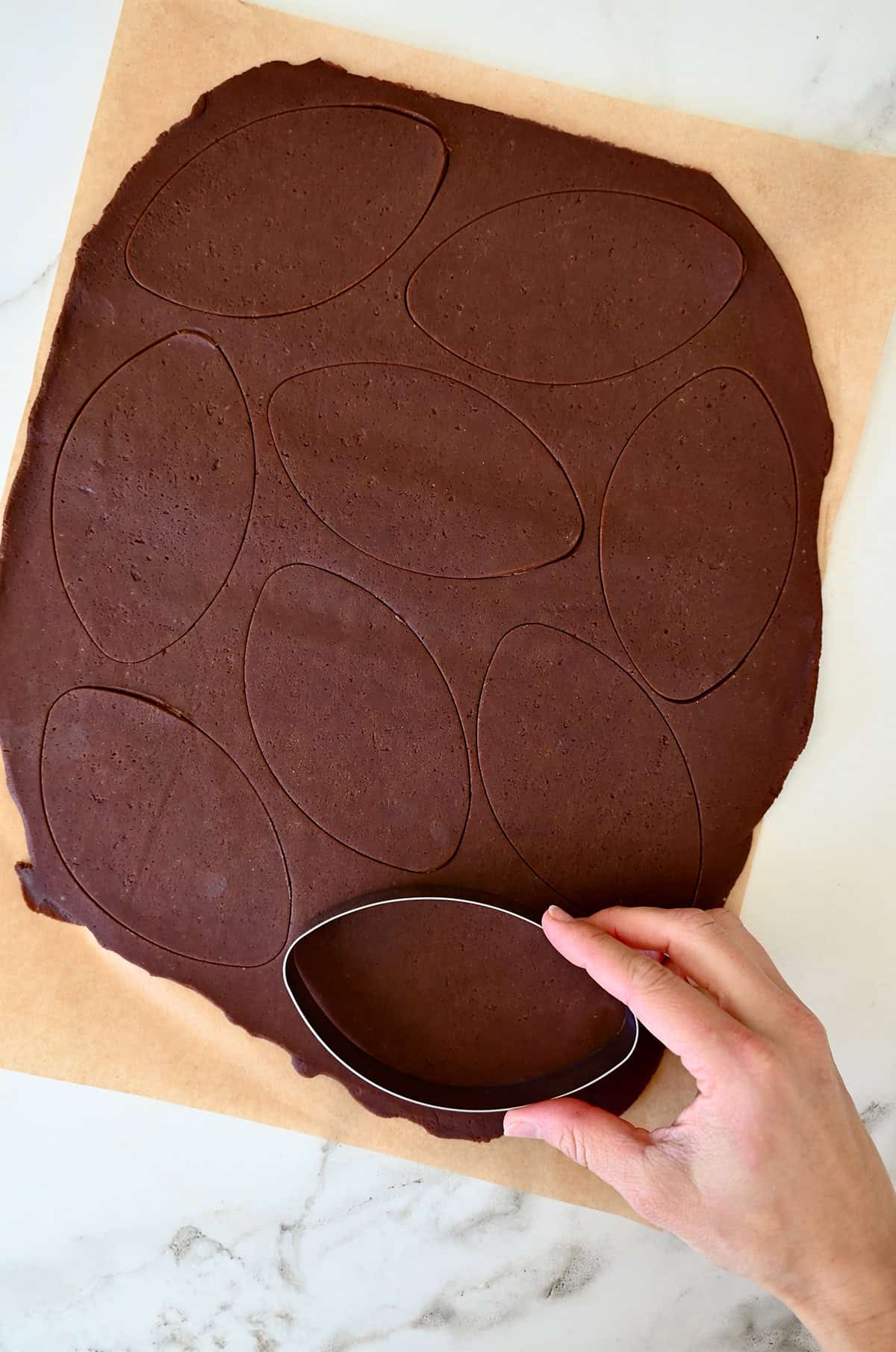 Using a football cookie cutter to cut out chocolate sugar cookie dough.