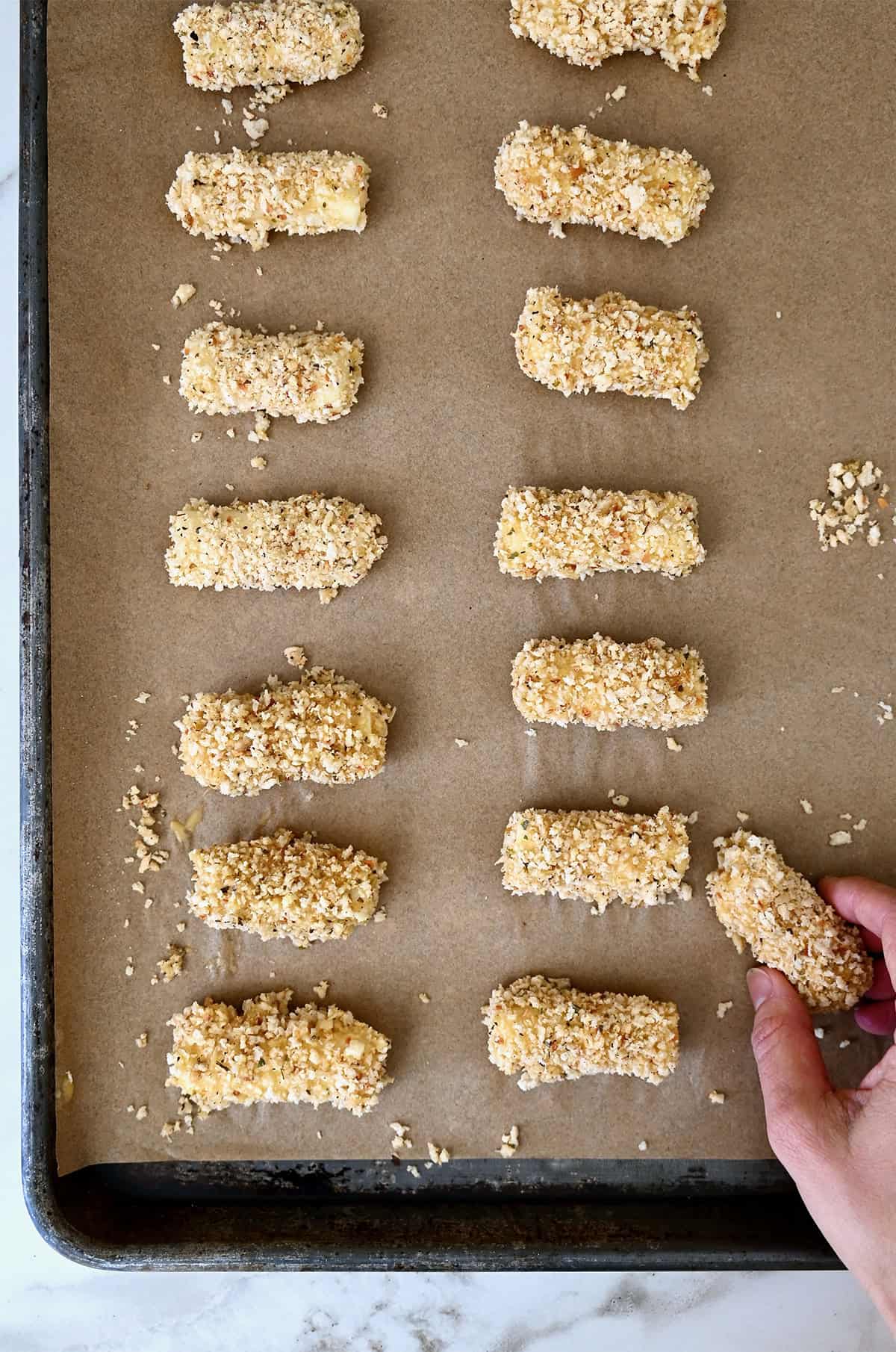 Frozen mozzarella sticks on a baking sheet lined with parchment paper.