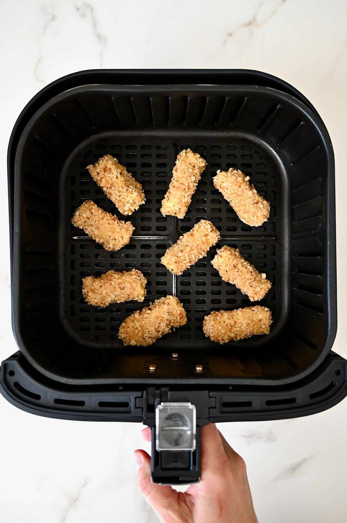 Homemade mozzarella sticks in an air fryer basket.