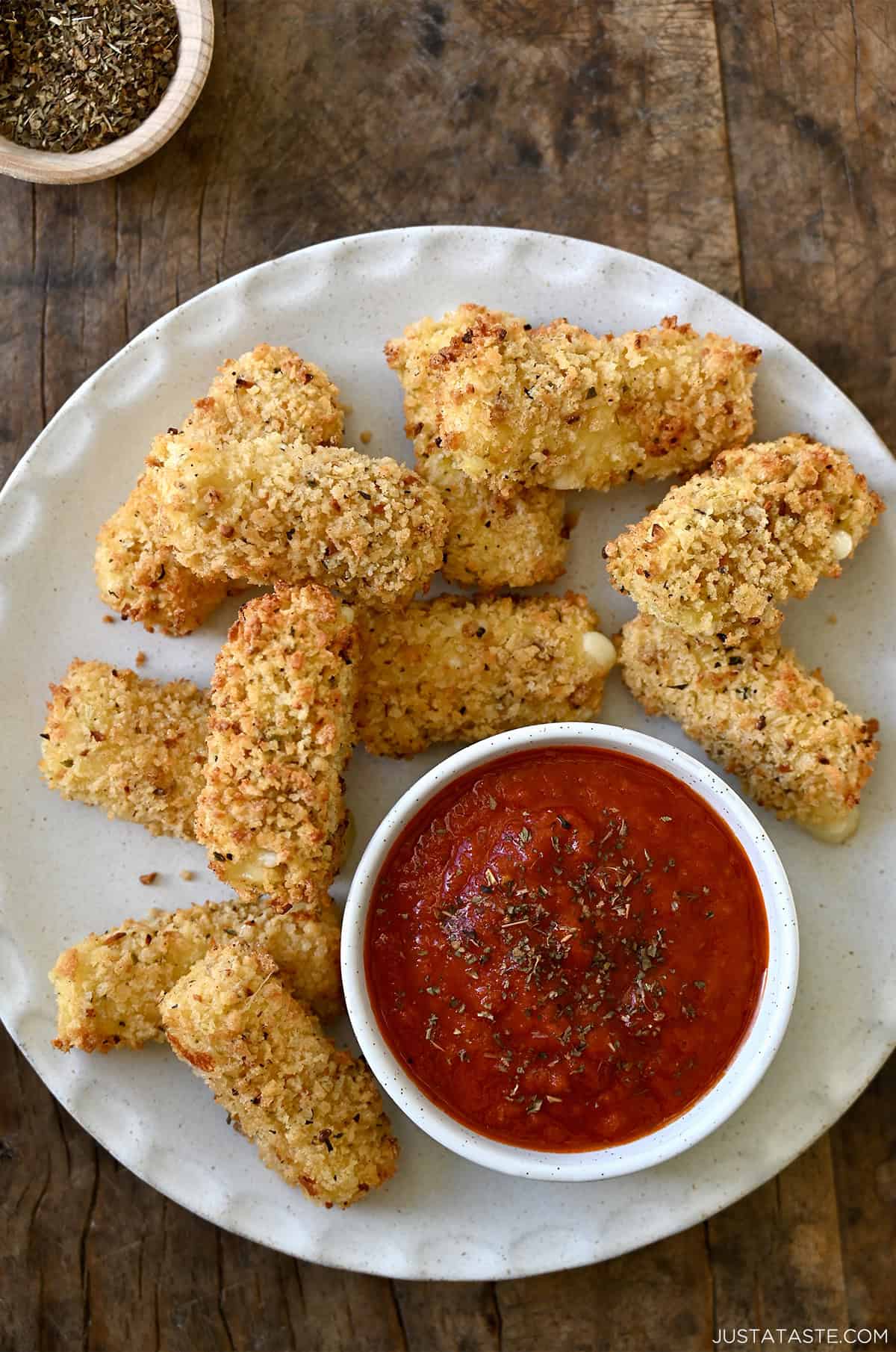 Golden brown mozzarella sticks made in an air fryer on a plate along with a small bowl containing marinara sauce.