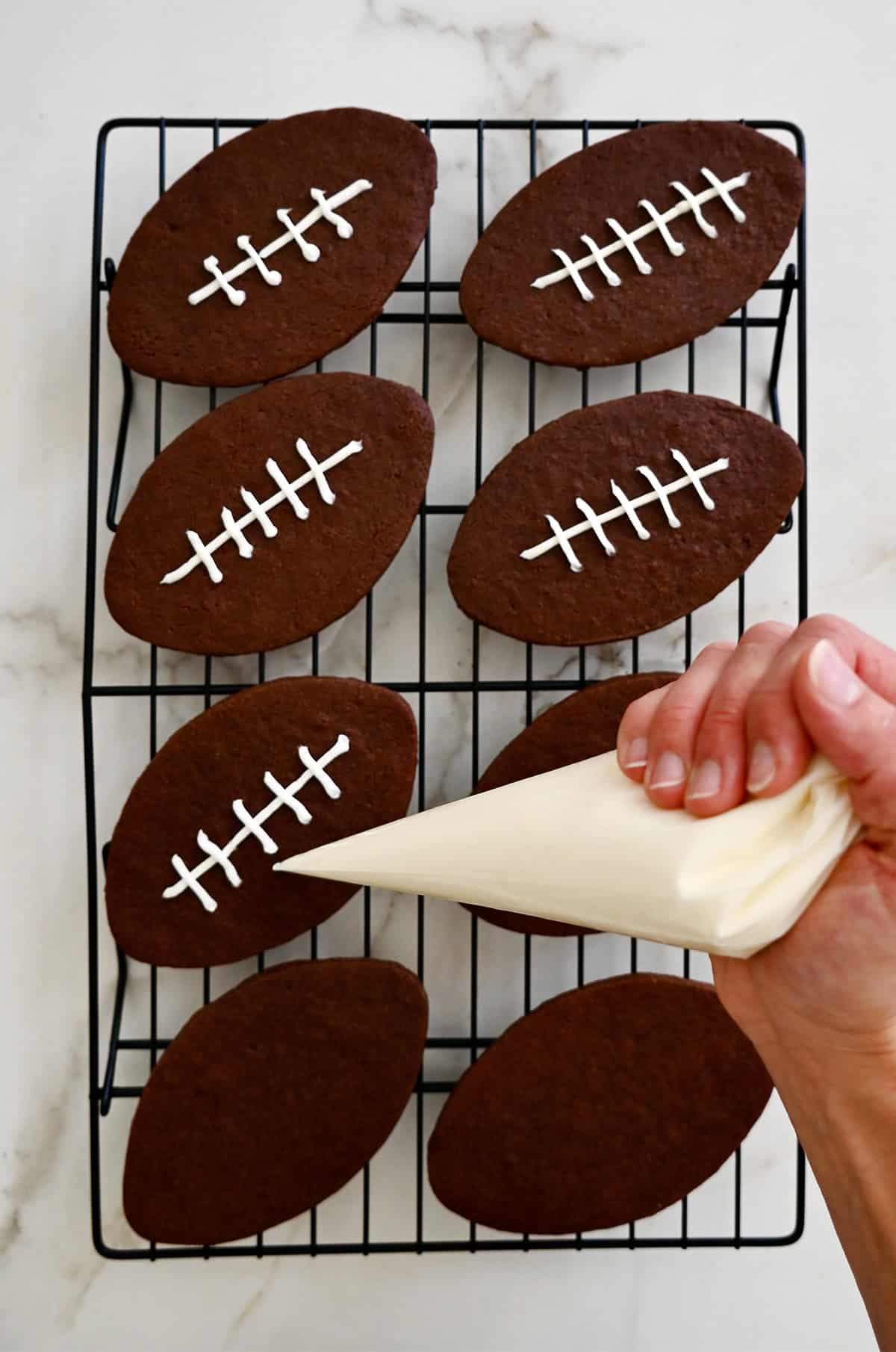 Piping cookie icing onto chocolate sugar cookies to look like football laces.