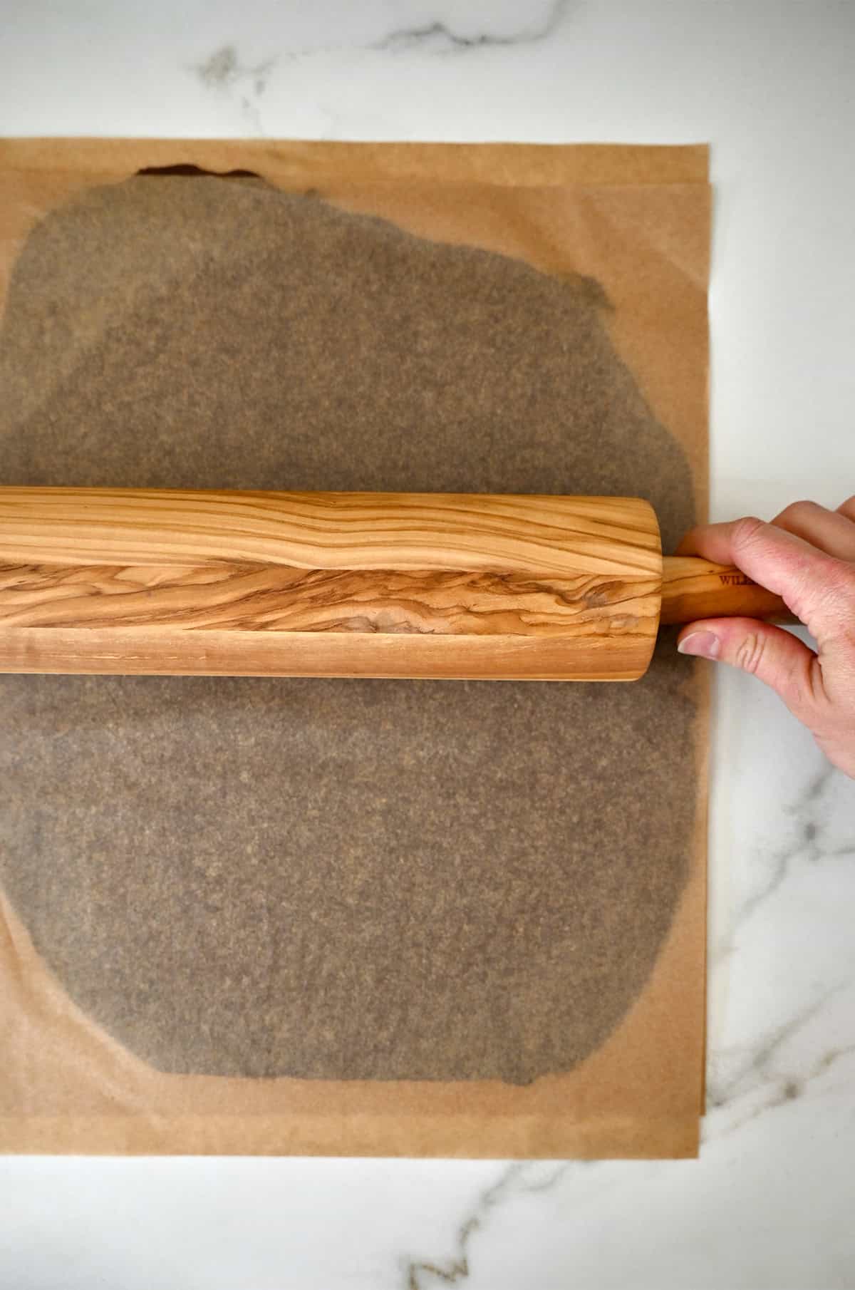 Rolling out chocolate sugar cookie dough between two sheets of parchment paper.