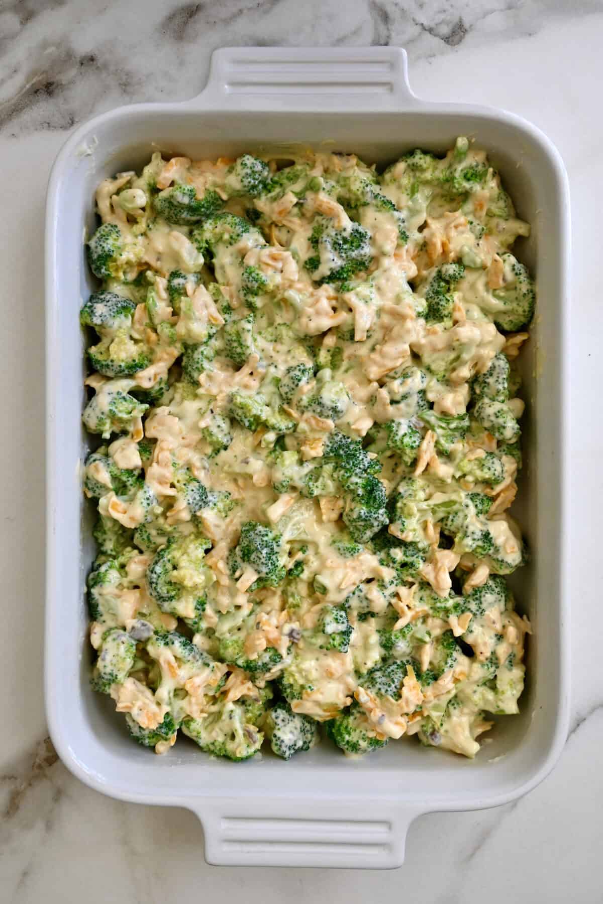 Unbaked broccoli cheddar cheese casserole in a white 9x13 baking dish.