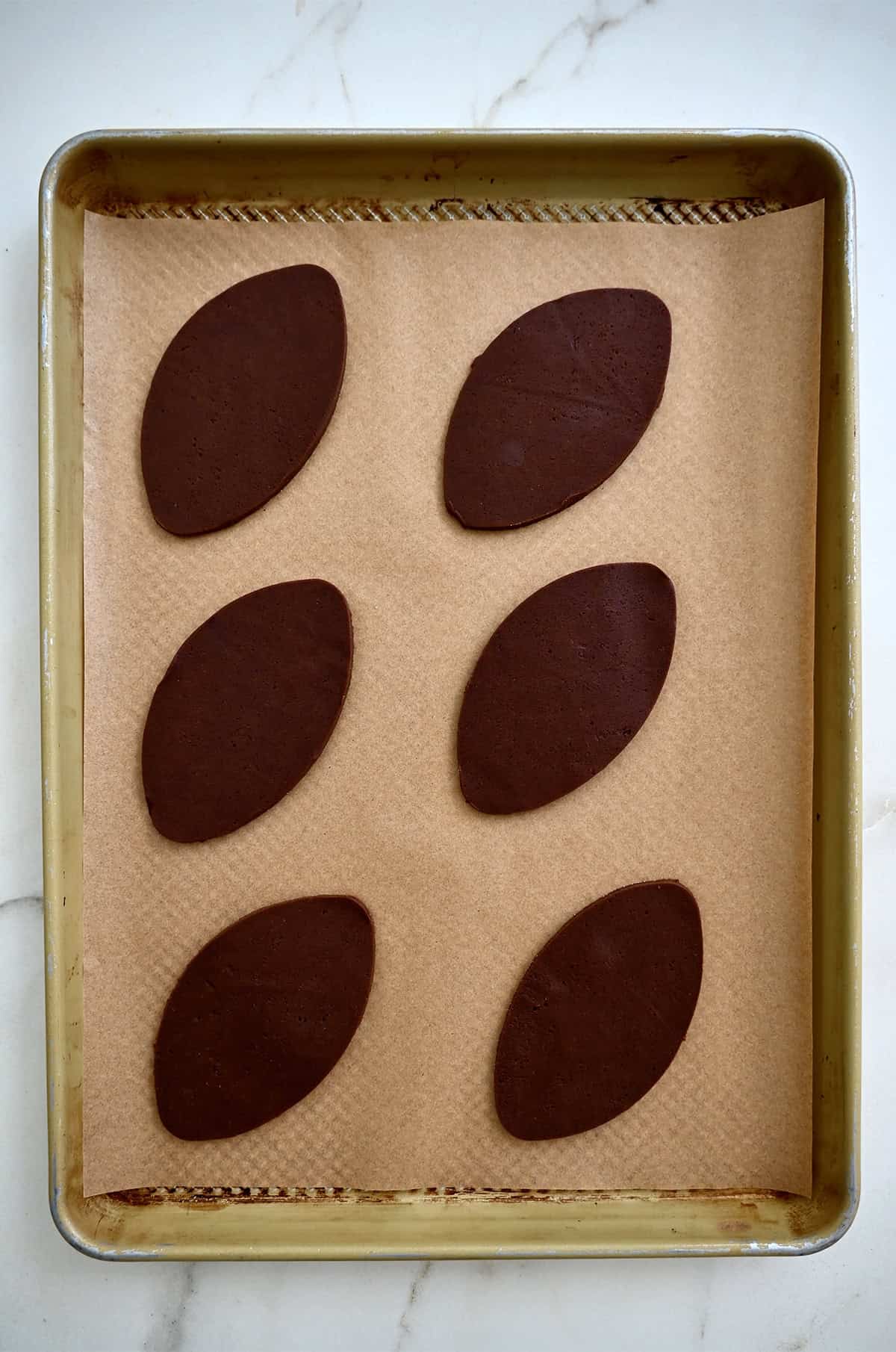 Unbaked football sugar cookies on a parchment paper-lined baking sheet.