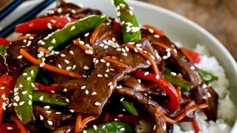 Beef stir-fry with veggies atop steamed white rice on a plate with chopsticks.