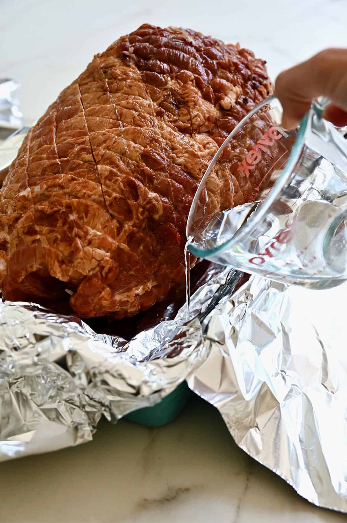 Įpilkite vandens į folijos išklotą skrudinimo keptuvę su kaulo kumpiu.