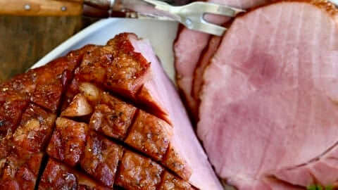 Baked ham with brown sugar glaze on a serving plate with roasted veggies.