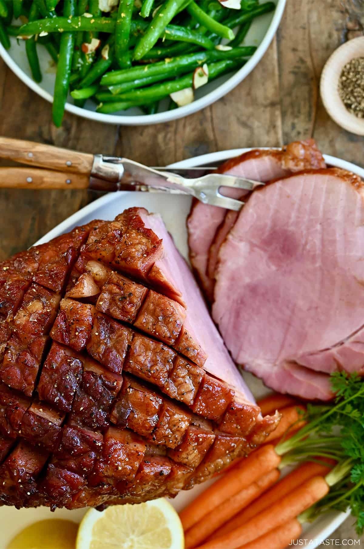 Baked ham with brown sugar glaze on a serving plate with roasted veggies.
